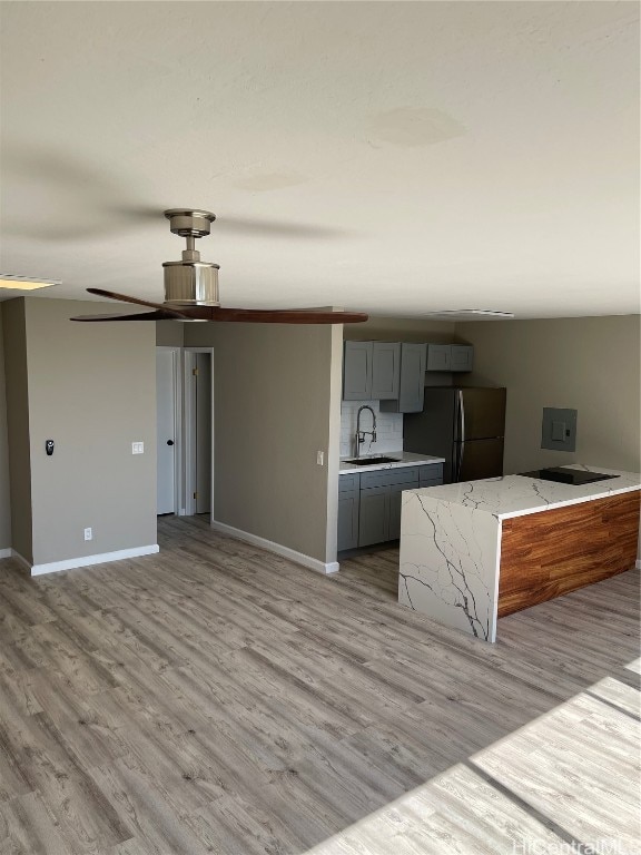 kitchen with gray cabinetry, light stone countertops, sink, stainless steel refrigerator, and light hardwood / wood-style flooring