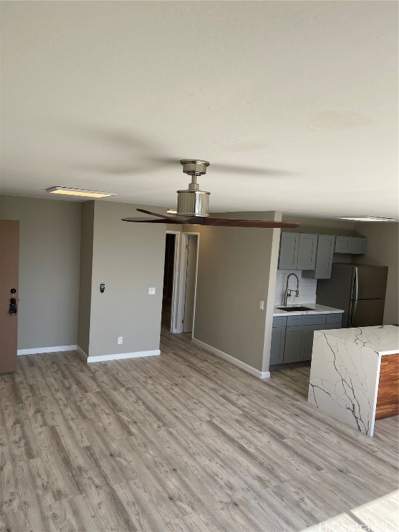 interior space with gray cabinetry, light stone countertops, sink, light wood-type flooring, and stainless steel fridge