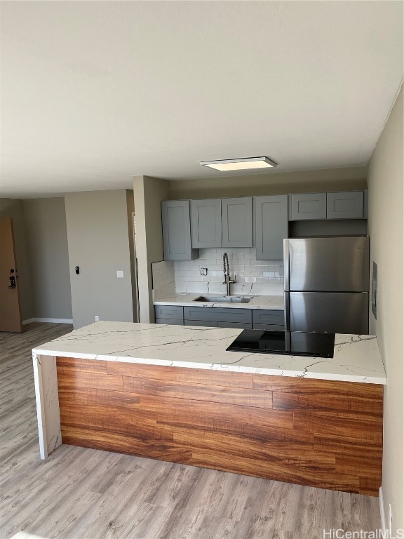 kitchen with light hardwood / wood-style floors, sink, light stone counters, and stainless steel fridge