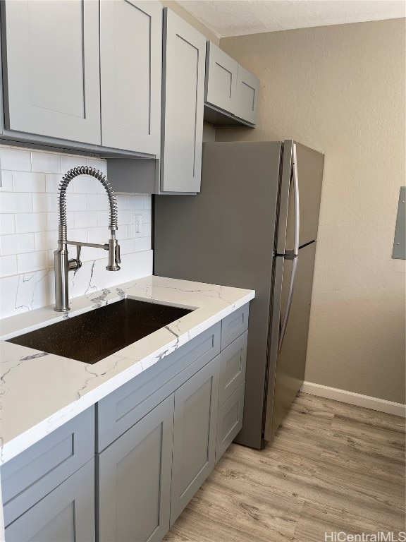 kitchen with gray cabinetry, sink, light wood-type flooring, light stone counters, and decorative backsplash