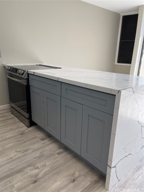 kitchen featuring gray cabinets, light stone counters, stainless steel range with electric stovetop, and light wood-type flooring