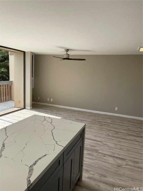 kitchen with light hardwood / wood-style floors, light stone countertops, and ceiling fan