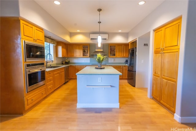 kitchen featuring stainless steel appliances, wall chimney range hood, sink, decorative light fixtures, and a kitchen island