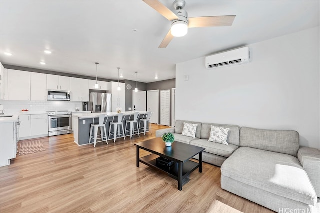 living room with an AC wall unit, light hardwood / wood-style floors, and ceiling fan