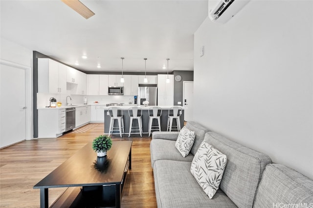 living room featuring sink, light wood-type flooring, and a wall unit AC