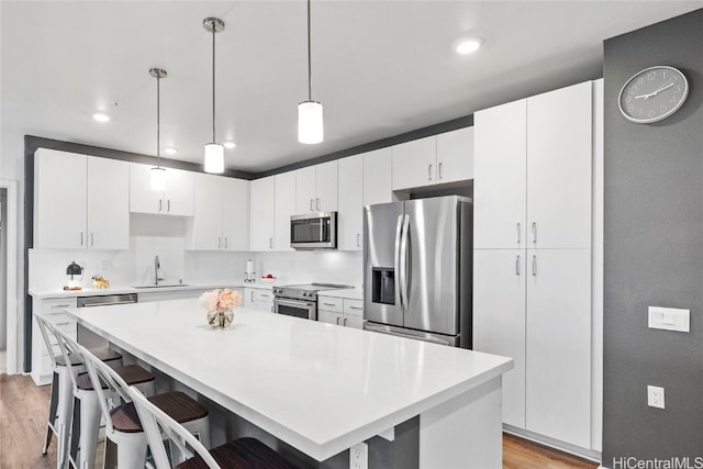 kitchen featuring light hardwood / wood-style flooring, white cabinetry, stainless steel appliances, and a kitchen bar