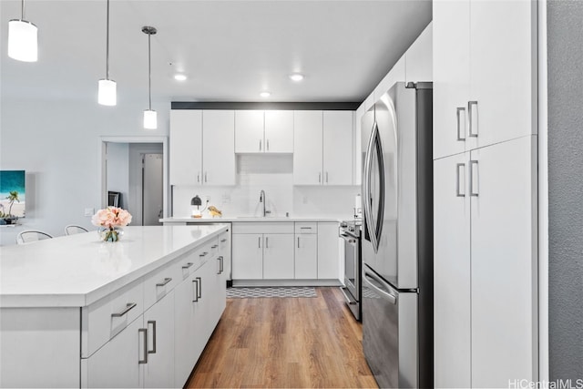 kitchen with white cabinetry, light hardwood / wood-style flooring, stainless steel appliances, and decorative light fixtures