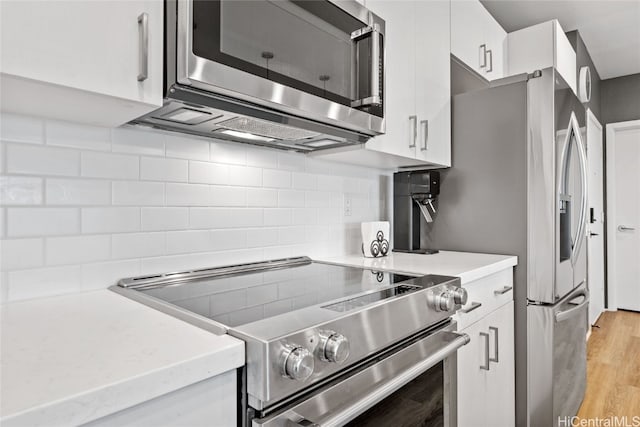 kitchen featuring backsplash, white cabinets, stainless steel appliances, and light hardwood / wood-style floors