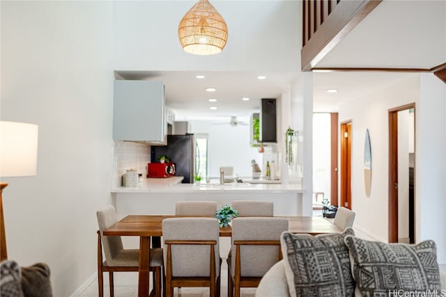 kitchen with exhaust hood, kitchen peninsula, tasteful backsplash, white cabinetry, and stainless steel refrigerator