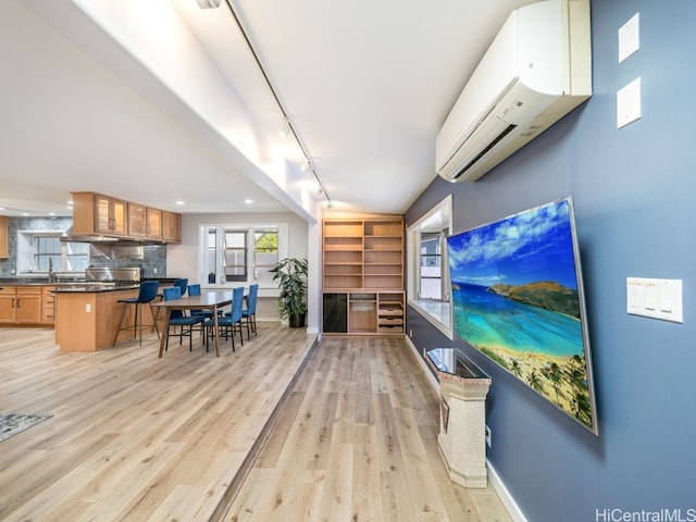 living room featuring a wall unit AC, rail lighting, and light hardwood / wood-style floors