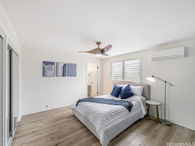 bedroom featuring ceiling fan, light hardwood / wood-style flooring, a wall unit AC, ensuite bathroom, and a closet