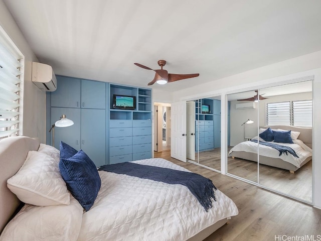 bedroom with a wall mounted air conditioner, two closets, light hardwood / wood-style flooring, and ceiling fan