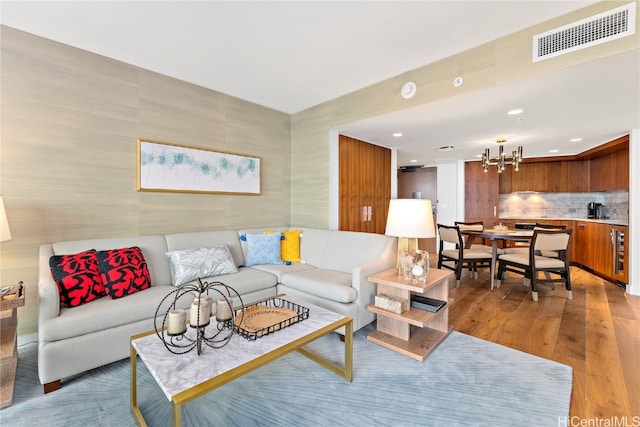 living room featuring wine cooler, wood-type flooring, and an inviting chandelier