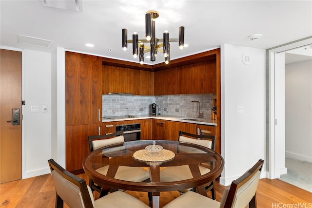 kitchen with black appliances, sink, light wood-type flooring, a notable chandelier, and decorative backsplash