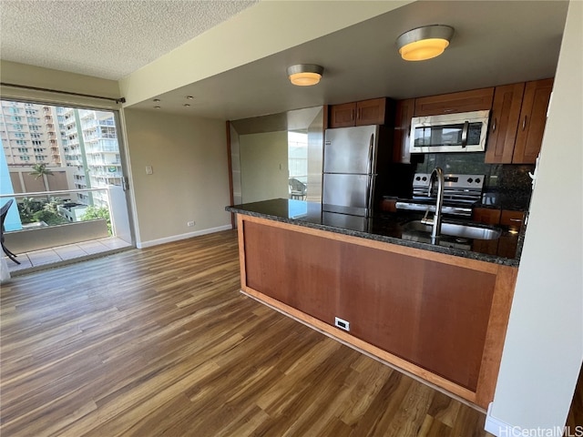 kitchen featuring decorative backsplash, dark wood-type flooring, dark stone countertops, sink, and appliances with stainless steel finishes