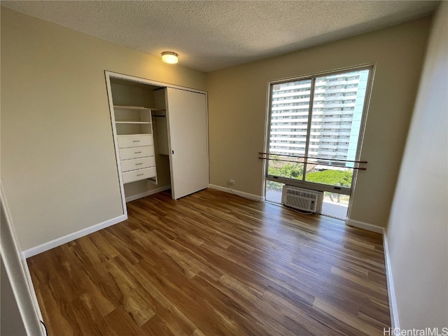 unfurnished bedroom featuring a closet, dark hardwood / wood-style floors, a wall mounted AC, and a textured ceiling