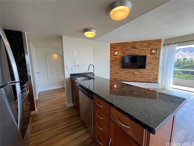 kitchen featuring sink, a textured ceiling, stainless steel appliances, dark stone counters, and hardwood / wood-style flooring