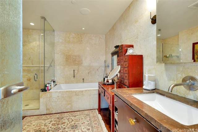 bathroom featuring separate shower and tub, vanity, and tile walls