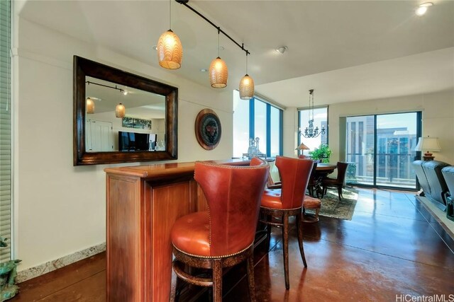 bar with rail lighting, decorative light fixtures, an inviting chandelier, and plenty of natural light