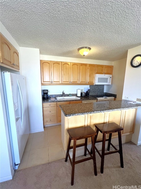 kitchen featuring sink, a kitchen bar, light colored carpet, and white appliances