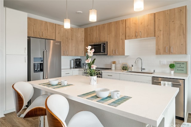 kitchen featuring sink, hanging light fixtures, stainless steel appliances, hardwood / wood-style floors, and a kitchen island