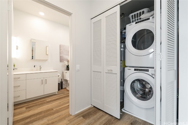 laundry area with sink, stacked washing maching and dryer, and light hardwood / wood-style floors