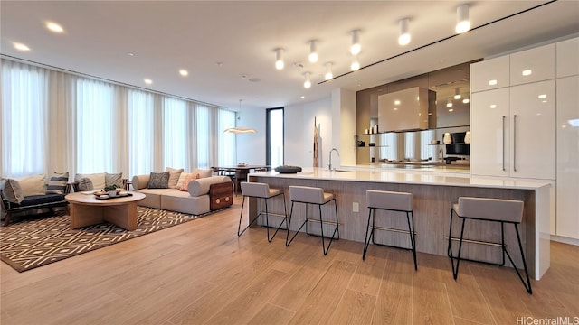 kitchen featuring light hardwood / wood-style floors, white cabinets, a large island with sink, and a breakfast bar area