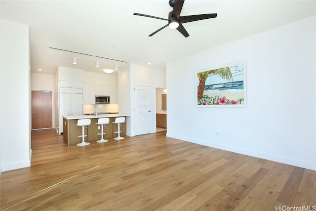 living room with rail lighting, sink, light wood-type flooring, and ceiling fan