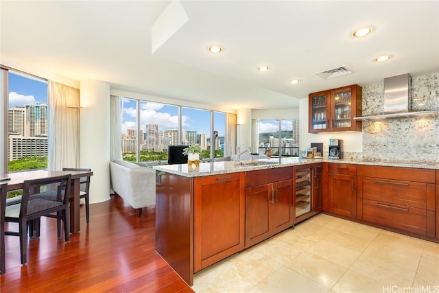 kitchen featuring kitchen peninsula, plenty of natural light, wall chimney exhaust hood, and beverage cooler