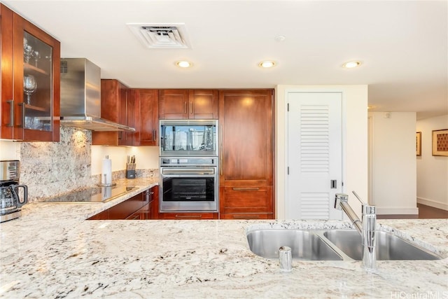 kitchen with black electric stovetop, light stone counters, wall chimney range hood, sink, and oven