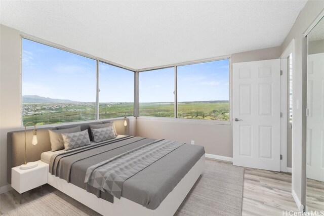 bedroom with a textured ceiling, hardwood / wood-style floors, a mountain view, and multiple windows