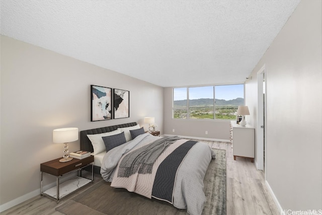 bedroom featuring a mountain view, light wood-type flooring, and a textured ceiling