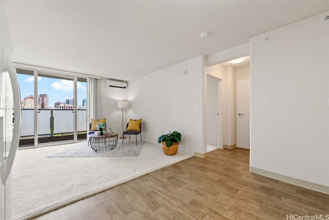 sitting room with light hardwood / wood-style floors, a wall mounted AC, a textured ceiling, and expansive windows