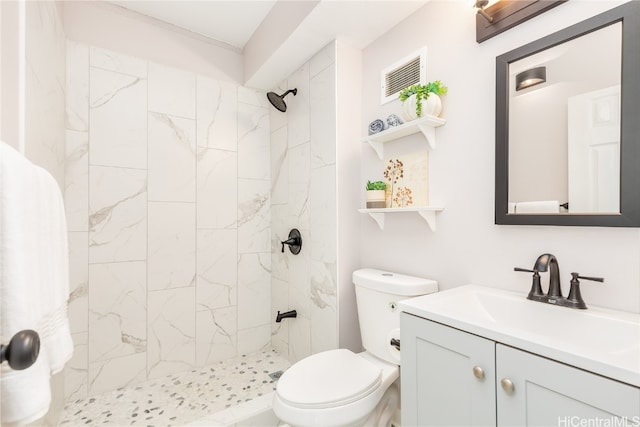 bathroom featuring vanity, a tile shower, and toilet