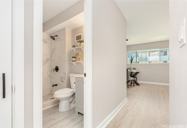 bathroom with toilet, hardwood / wood-style flooring, and tiled shower