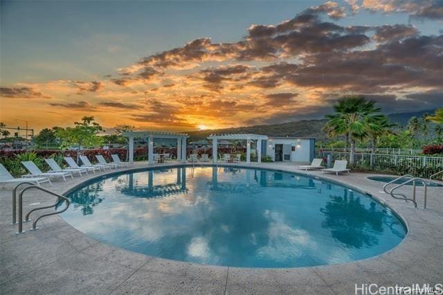 pool at dusk with a patio area and a pergola