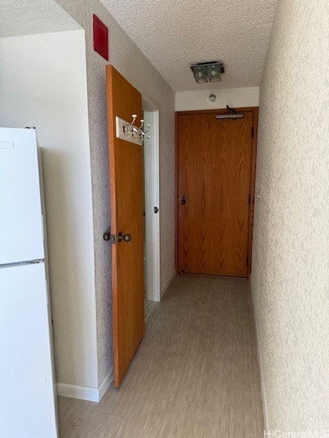 hallway with a textured ceiling and light wood-type flooring