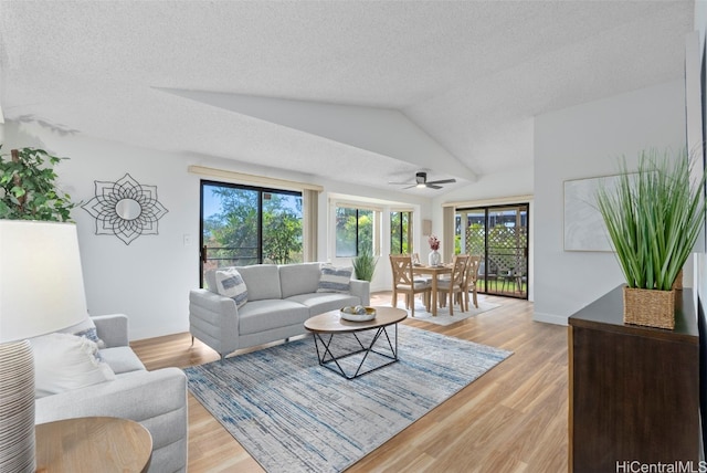 living room featuring light hardwood / wood-style flooring, a textured ceiling, ceiling fan, and vaulted ceiling