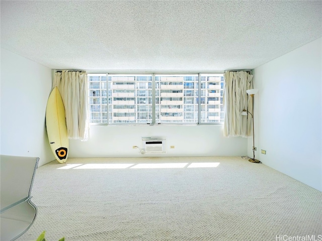 empty room with an AC wall unit, a textured ceiling, and light colored carpet