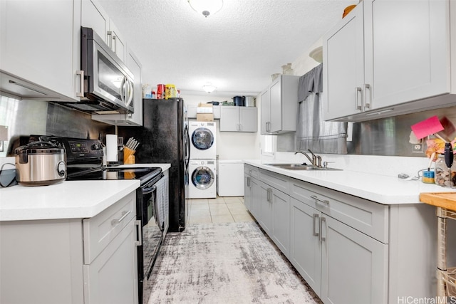 kitchen featuring light tile patterned floors, a textured ceiling, stacked washer / drying machine, black electric range, and sink