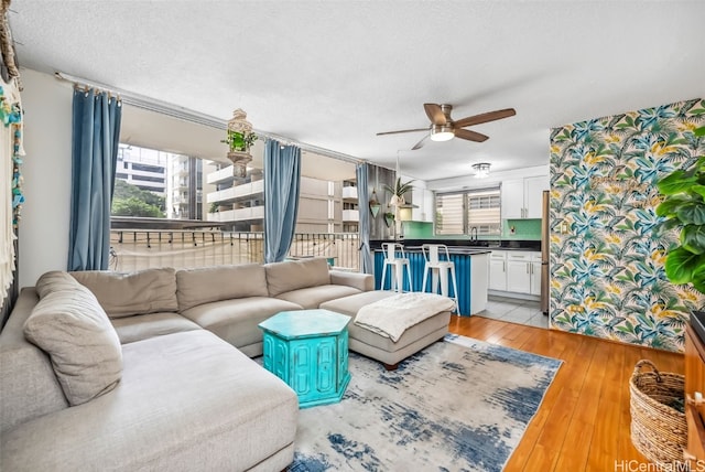 living room featuring light hardwood / wood-style floors, a textured ceiling, and ceiling fan