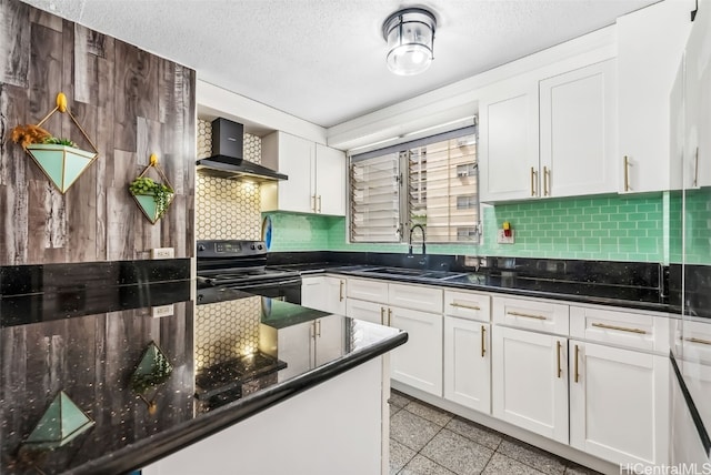 kitchen with wall chimney range hood, dark stone counters, sink, black electric range, and white cabinets