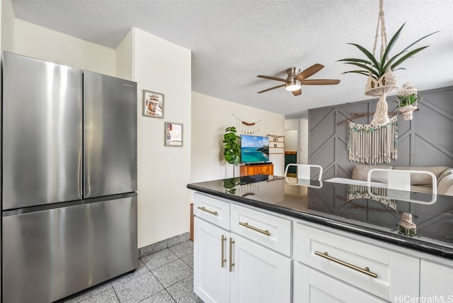 kitchen featuring white cabinets, ceiling fan, a textured ceiling, and stainless steel refrigerator