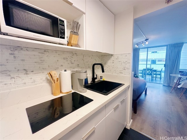 kitchen with tasteful backsplash, sink, black electric cooktop, hardwood / wood-style floors, and white cabinets