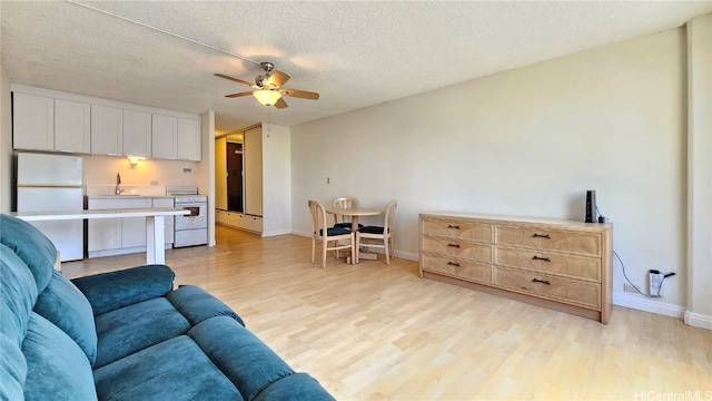 living room featuring ceiling fan, a textured ceiling, sink, and light wood-type flooring