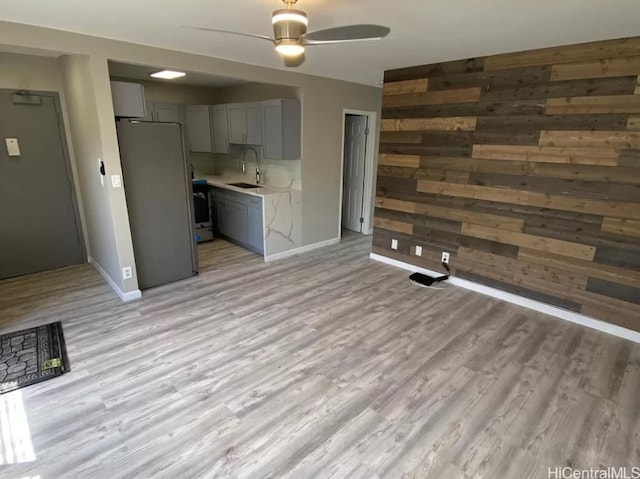 unfurnished living room featuring ceiling fan, sink, wood walls, and light hardwood / wood-style floors