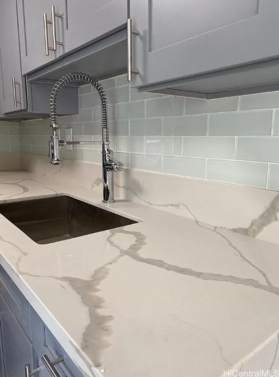 interior details with light stone countertops, gray cabinetry, tasteful backsplash, and sink