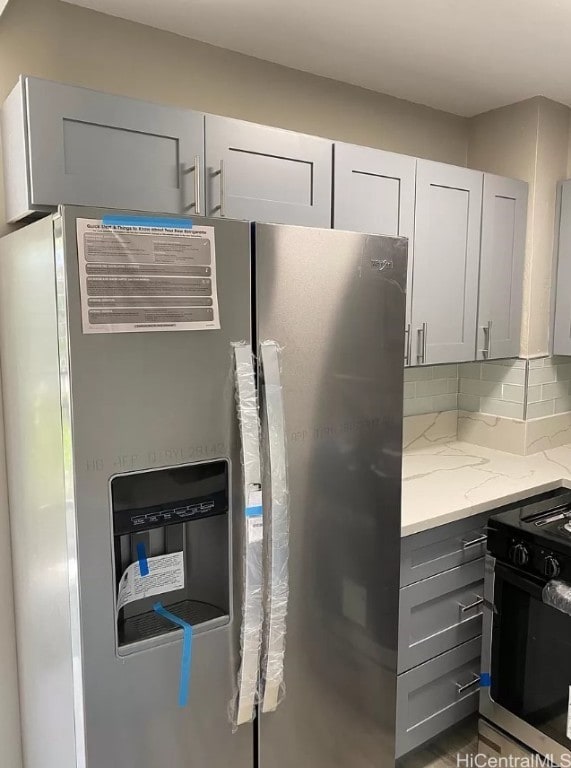 kitchen featuring light stone counters, backsplash, stainless steel fridge, and stove