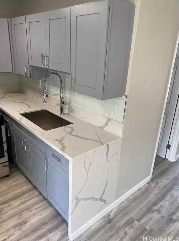 kitchen with tasteful backsplash, gray cabinets, sink, light wood-type flooring, and light stone counters