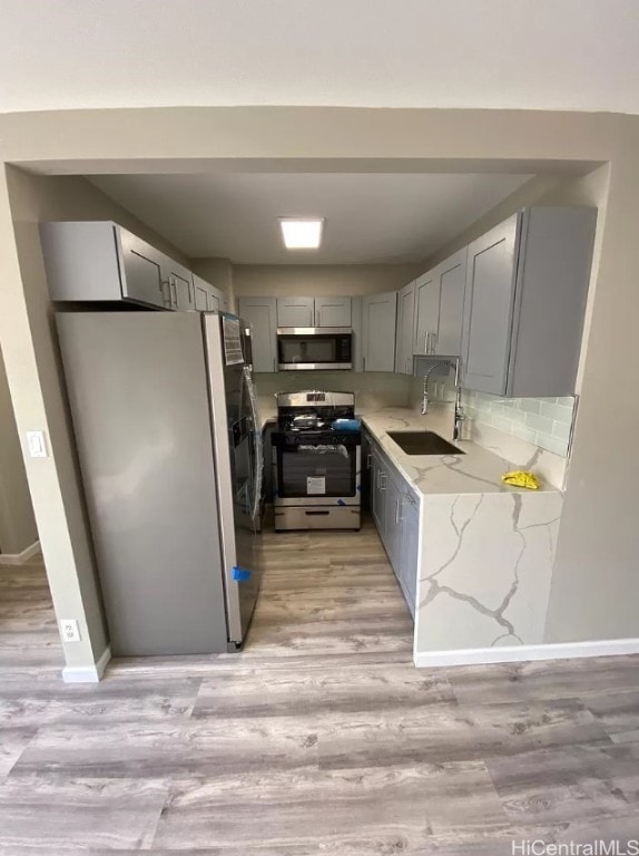 kitchen featuring sink, light hardwood / wood-style flooring, gray cabinetry, stainless steel appliances, and light stone counters